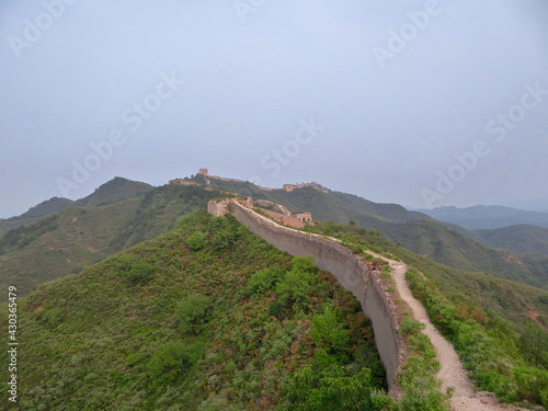 A panoramic view on an unrenewed Gubeikou part of Great Wall of China. The wall is spreading on tops of mountains. Many watchtowers on the peaks. Dense forest around it. World wonder. Tradition