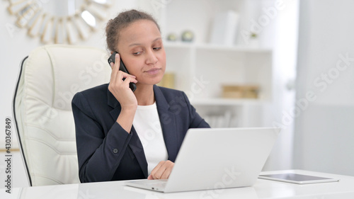 African Businesswoman with Laptop Talking on Phone in Office 