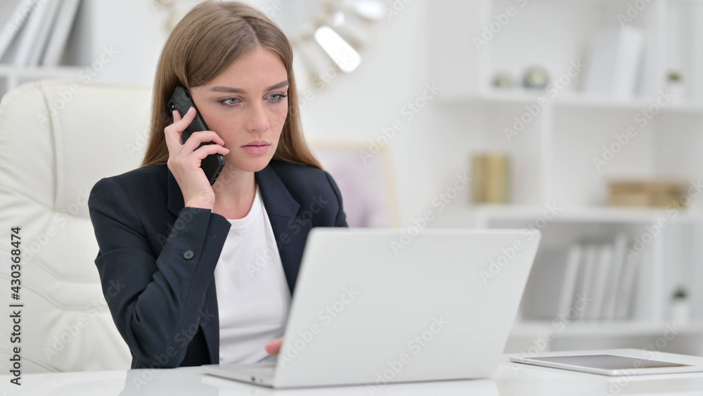 Serious Businesswoman with Laptop Talking on Phone in Office Serious Businesswoman with Laptop Talking on Phone in Office