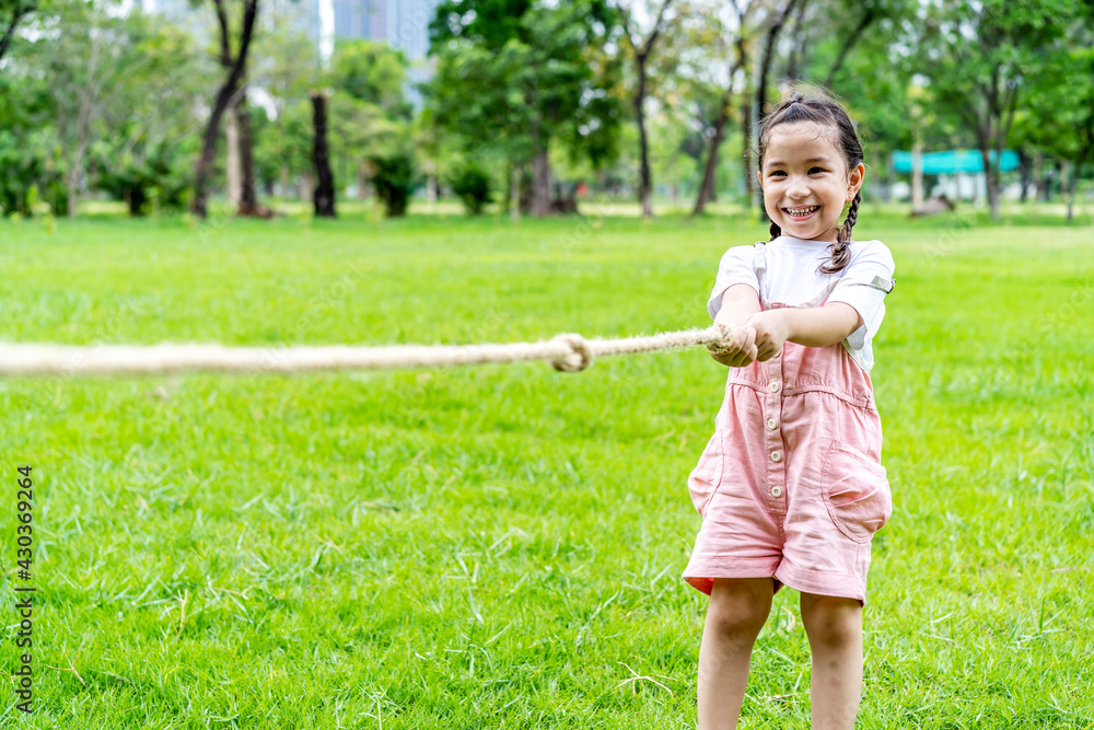 Cheerful child girl having fun to playing tug of war at the park, smiling girl pulling a rope on the green lawn, children sport concep Cheerful child girl having fun to playing tug of war at the park, smiling girl pulling a rope on the green lawn, children sport concep