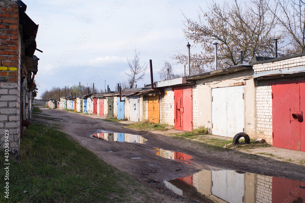 Brick garages with bright metal doors in the city on a spring day with puddles on the road after rain. Garage cooperative Brick garages with bright metal doors in the city on a spring day with puddles on the road after rain. Garage cooperative