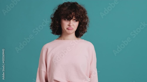The offended woman showing a tongue and looking away while standing in the blue studio