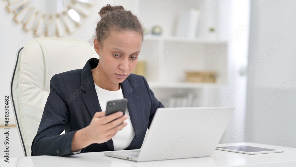 African Businesswoman using Smartphone and Laptop in Office African Businesswoman using Smartphone and Laptop in Office