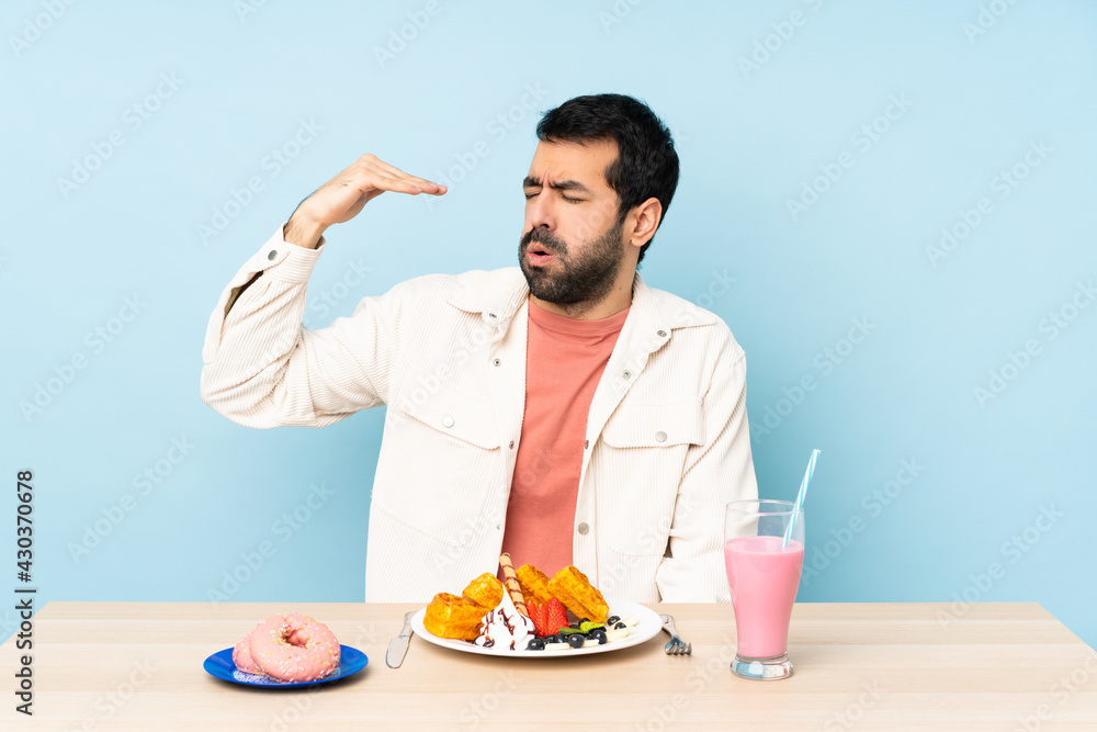 Man at a table having breakfast waffles and a milkshake with tired and sick expression Man at a table having breakfast waffles and a milkshake with tired and sick expression