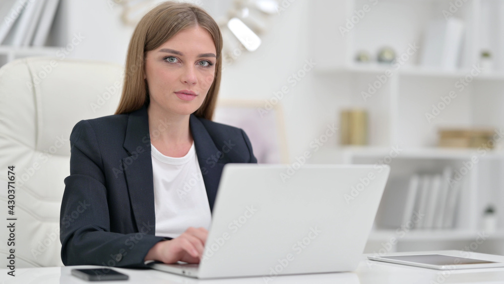 Young Businesswoman with Laptop Looking at Camera in Office 