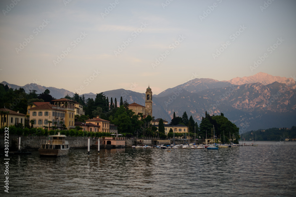 Obraz premium Evening on lake with warm sunset colours and old italian village with church tower harbor full of yachts