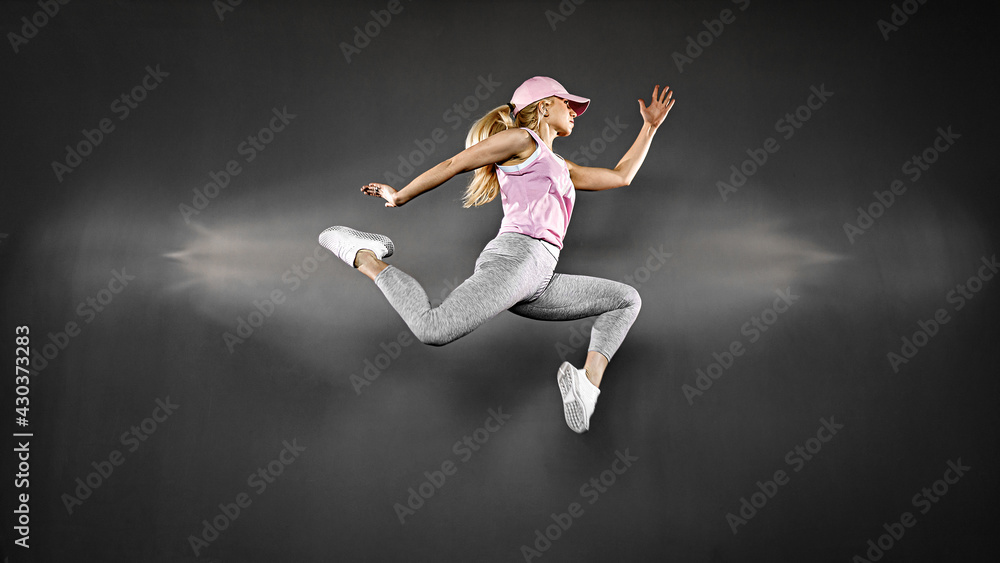 Young woman with fit body jumping and running against grey backg