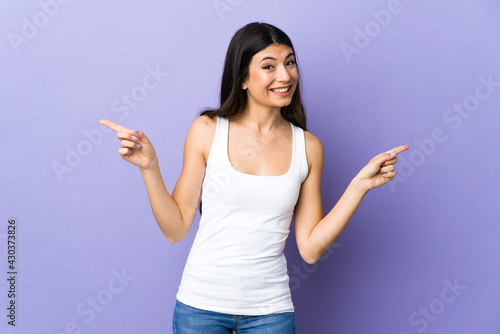 Young brunette woman over isolated purple background pointing finger to the laterals and happy