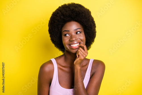 Photo of dreamy cute dark skin girl look empty space bite nail finger isolated on vivid yellow color background