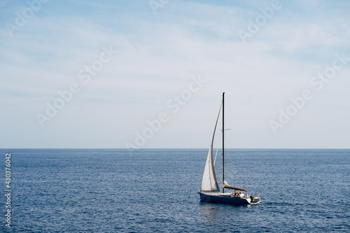 Small boat with a white sail fluttering in the wind sails on the sea © Nadtochiy