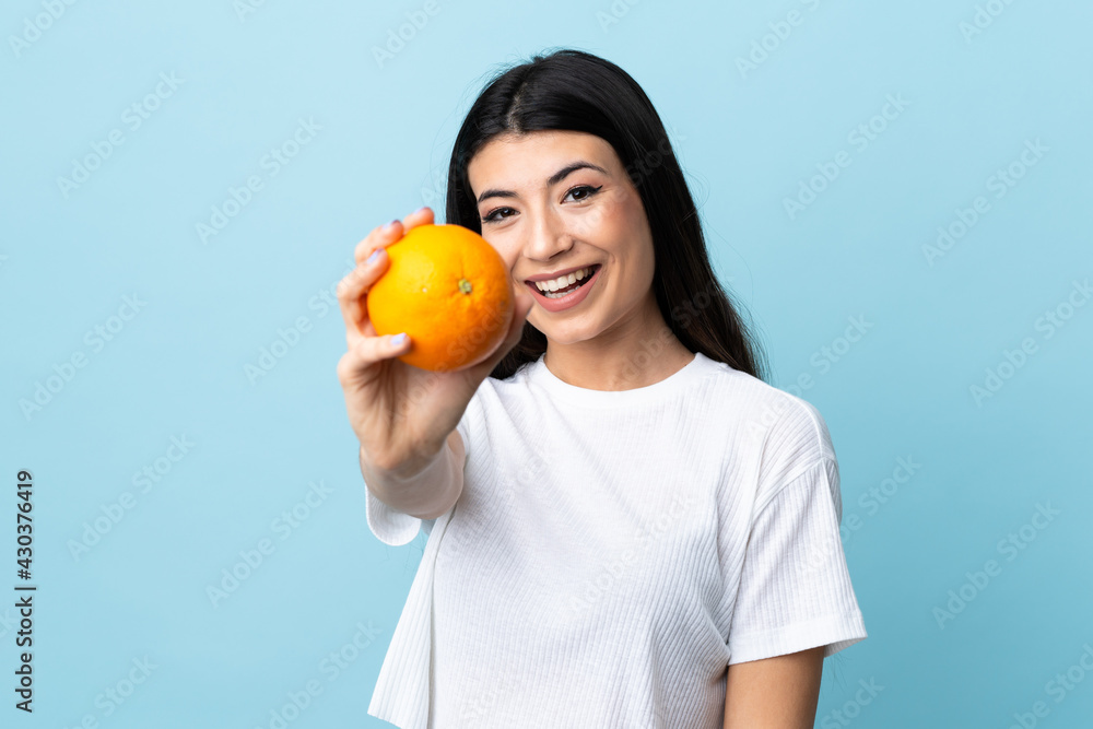 Young brunette girl over isolated blue background holding an orange Young brunette girl over isolated blue background holding an orange
