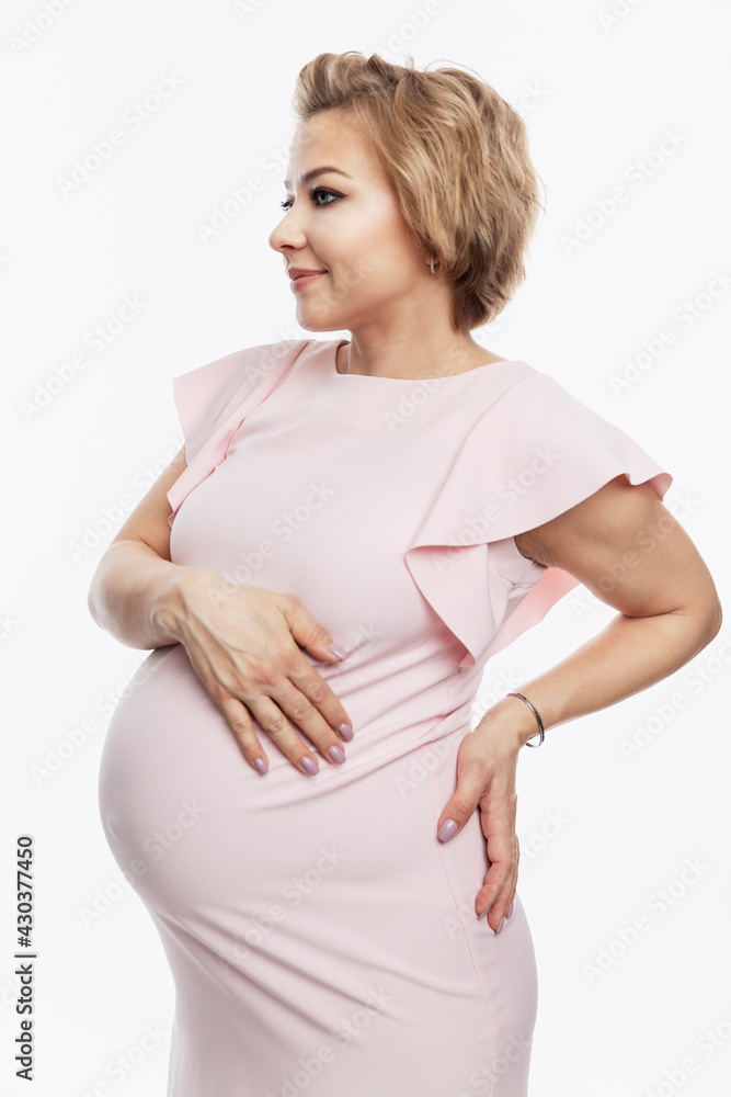 Happy smiling pregnant blonde woman stands and touches big belly. Waiting for the birth of a baby. White background. Vertical. Happy smiling pregnant blonde woman stands and touches big belly. Waiting for the birth of a baby. White background. Vertical.