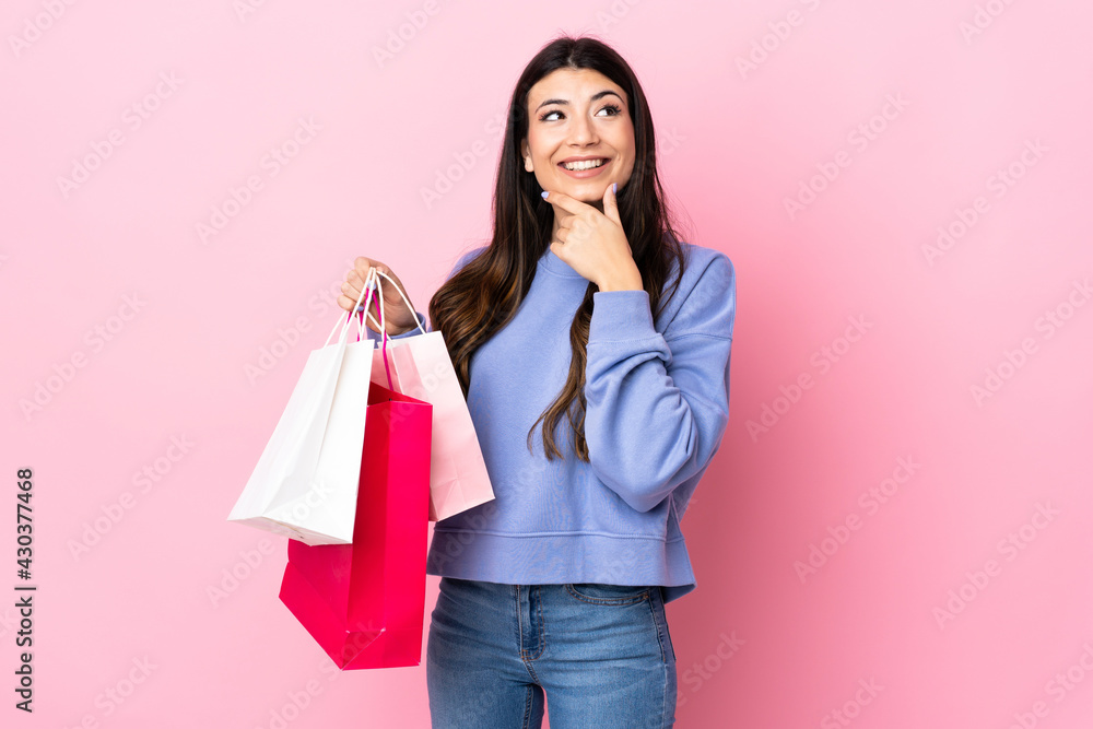 Young brunette girl over isolated pink background holding shopping bags and thinking