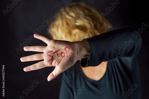 A blonde woman dressed in black covers her face with a hand on which she has written the word stop with a red marker, to stop violence against women