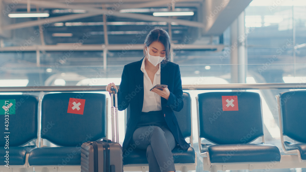 Asian business lady traveller wear suit sitting with suitcase and use smart phone chat message in bench wait for flight at airport. Business travel commuter in covid pandemic, Business travel concept. Asian business lady traveller wear suit sitting with suitcase and use smart phone chat message in bench wait for flight at airport. Business travel commuter in covid pandemic, Business travel concept.