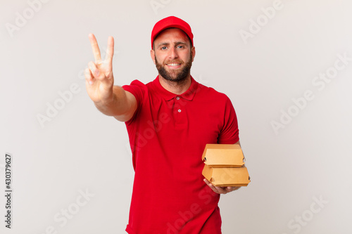 young handsome man smiling and looking friendly, showing number two burger delivering concept photo