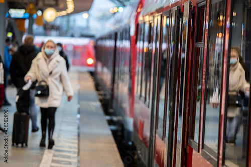 Frau mit Koffer und Maske zum Schutz vor Corona am Bahngleis im Hauptbahnhof Köln bei der Einfahrt des Zuges