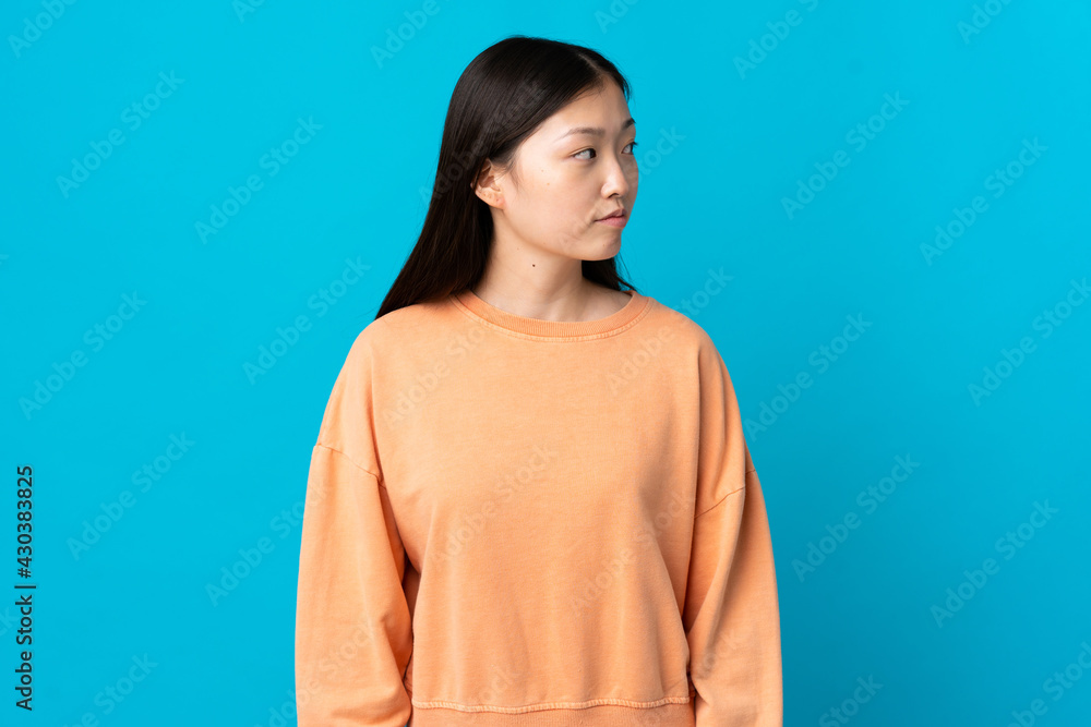 Young Chinese girl over isolated blue background looking to the side Young Chinese girl over isolated blue background looking to the side