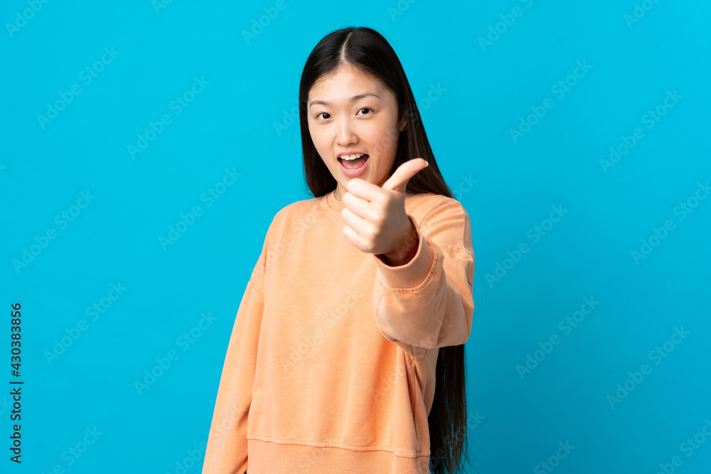 Young Chinese girl over isolated blue background with thumbs up because something good has happened Young Chinese girl over isolated blue background with thumbs up because something good has happened