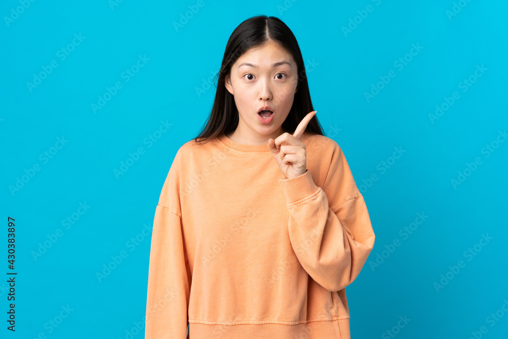 Young Chinese girl over isolated blue background intending to realizes the solution while lifting a finger up