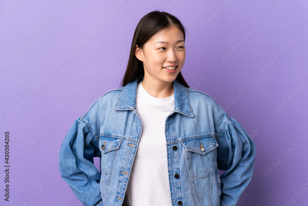 Young Chinese girl over isolated purple background posing with arms at hip and smiling Young Chinese girl over isolated purple background posing with arms at hip and smiling