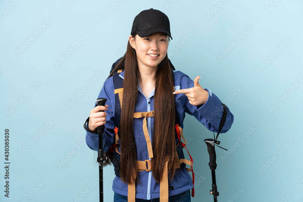 Young Chinese girl with backpack and trekking poles over isolated blue background proud and self-satisfied Young Chinese girl with backpack and trekking poles over isolated blue background proud and self-satisfied