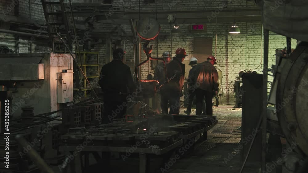 Team of professional foundry men in hard hats and uniforms carrying melted iron working together Team of professional foundry men in hard hats and uniforms carrying melted iron working together