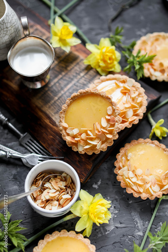 Lemon mini tarts on a wooden board on a gray table. Sweets and flowers. Bright yellow dessert.