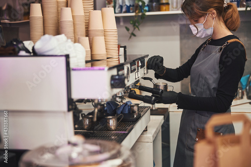 Busy female barista operating coffee machine and making hot beverage