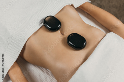 Hot stone massage on the belly. Close-up of the lava stone on the skin and abdomen. Treatment for the improvement of blood circulation, elimination of toxins and muscle relaxation.