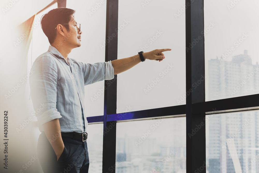 Businessman standing in front of window with hand pointing outside. Businessman standing in front of window with hand pointing outside.