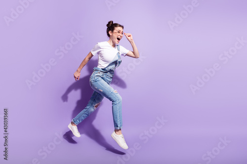 Full length profile side photo of young girl happy smile jump go walk run hurry isolated over violet color background