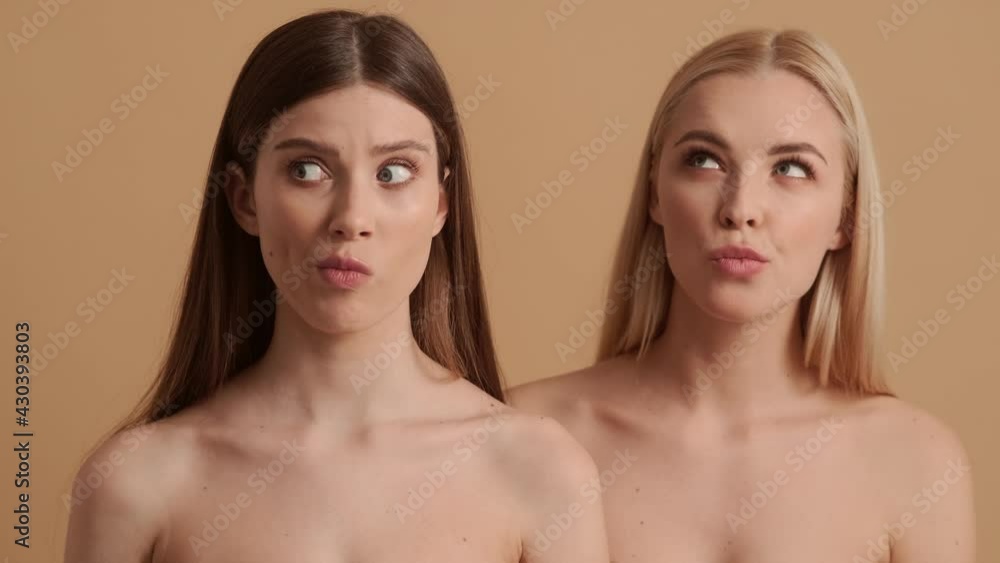 Happy young half-naked women are dreaming and thinking about something standing isolated over a beige background in the studio Happy young half-naked women are dreaming and thinking about something standing isolated over a beige background in the studio