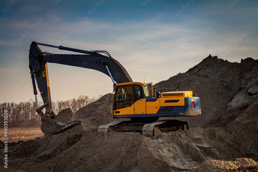 Obraz premium Large construction excavator yellow on a construction site in a quarry for quarrying. Yellow excavator on a construction site against blue sky.