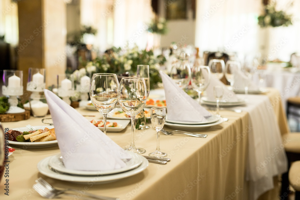 Close up of festive table setting with wine glasses, fresh flowers on beige tablecloth