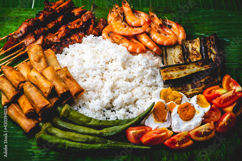 Boodle Fight- White Rice, Lumpiang Shanghai, Salted Egg, Tomato, Boiled Okra, Fried Eggplant, Shrimps, and Pork barbecue (flat lay close up)