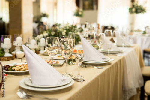Close up of festive table setting with wine glasses, fresh flowers on beige tablecloth