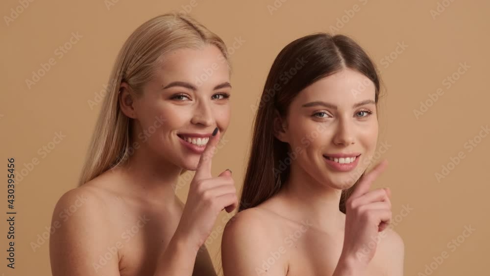Happy young half-naked women are doing silence gesture standing isolated over a beige background in the studio Happy young half-naked women are doing silence gesture standing isolated over a beige background in the studio