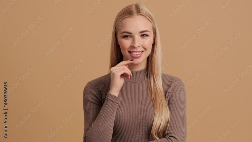 A dreaming young blond woman is standing isolated over a beige background in the studio A dreaming young blond woman is standing isolated over a beige background in the studio
