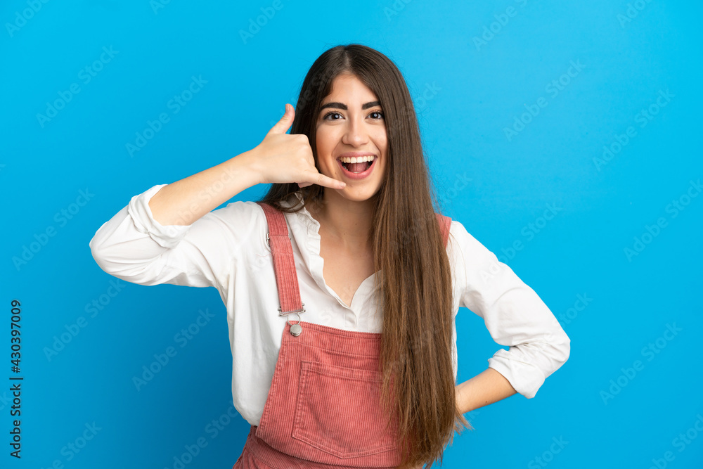 Young caucasian woman isolated on blue background making phone gesture. Call me back sign Young caucasian woman isolated on blue background making phone gesture. Call me back sign