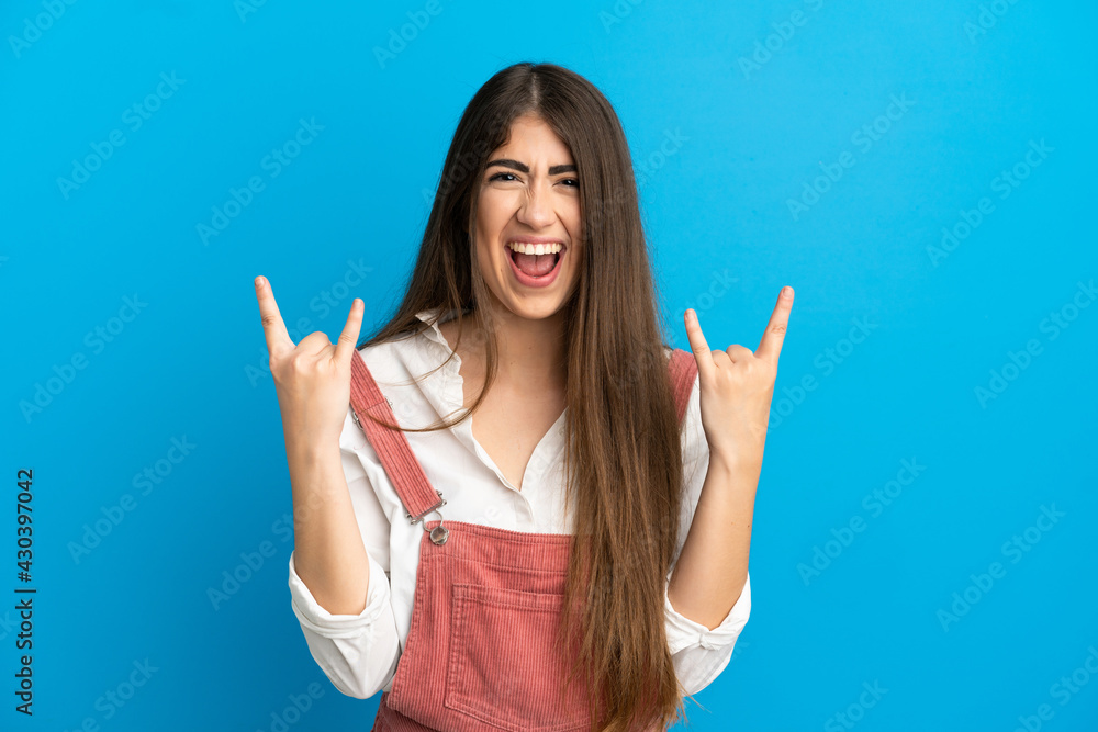 Young caucasian woman isolated on blue background making horn gesture Young caucasian woman isolated on blue background making horn gesture
