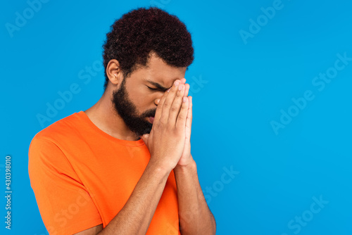 bearded african american man praying isolated on blue