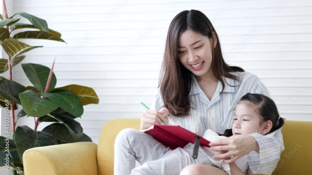 Cute child daughter is happy to write Drawing book with mother in living room at home during school holidays. Asian family activities. Child freedom of ideas. Kid girl having fun in room on leisure Cute child daughter is happy to write Drawing book with mother in living room at home during school holidays. Asian family activities. Child freedom of ideas. Kid girl having fun in room on leisure