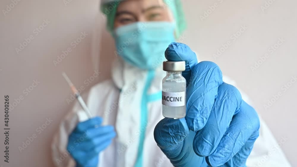 Healthcare worker in PPE suit holding a syringe and showing a bottle of covid-19 vaccine. Healthcare worker in PPE suit holding a syringe and showing a bottle of covid-19 vaccine.