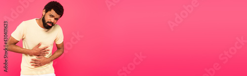 displeased african american man suffering from stomach ache isolated on pink, banner