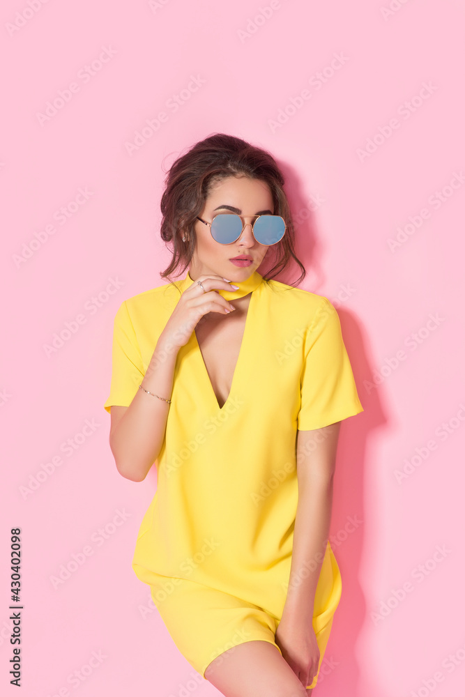 Beautiful girl in yellow dress wearing sunglasses posing, smiling on pink background in studio. Beautiful girl in yellow dress wearing sunglasses posing, smiling on pink background in studio.