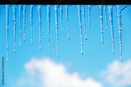 Icicles on a blue sky background with clouds. Spring or winter theme with transparent clear thawing ice shining in the sun. Frozen water  water drops  droplets  icicles  thaw.