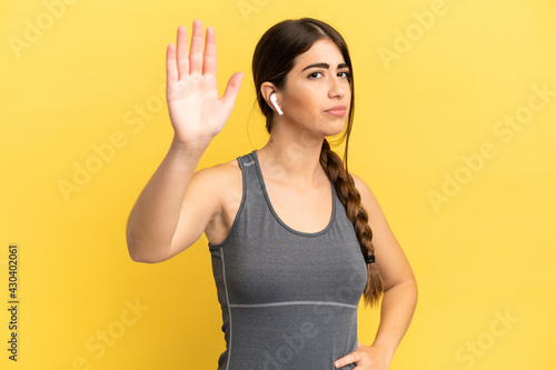 Sport caucasian woman isolated on yellow background making stop gesture and disappointed