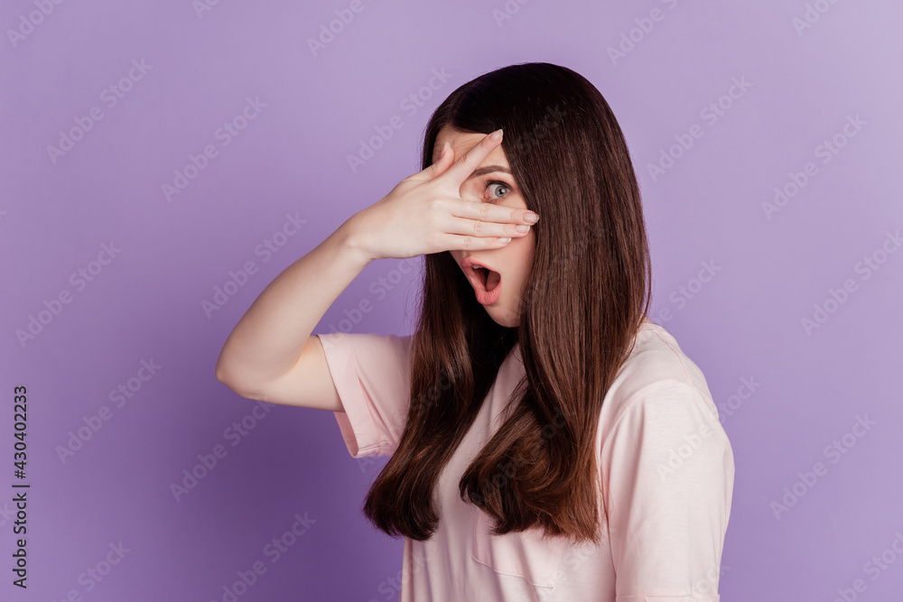 Portrait of shy young woman cover face peek through fingers open mouth on purple wall Portrait of shy young woman cover face peek through fingers open mouth on purple wall