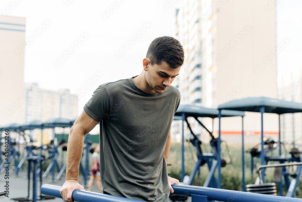 Young handsome man doing push-ups on the uneven bars outdoor. Sports, fitness, gymnastics workout Young handsome man doing push-ups on the uneven bars outdoor. Sports, fitness, gymnastics workout